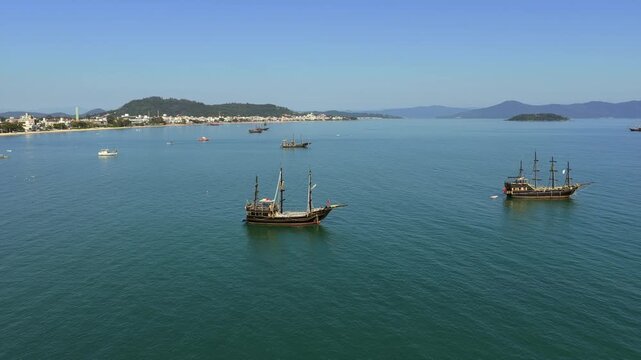 Pirate style tour ships in Cachoeira do Bom Jesus and Canasvieiras Florian&oacute;polis Santa Catarina Brazil on Ba&iacute;a Norte with calm sea and coastal skyline backed by Serra do Mar, static aerial shot