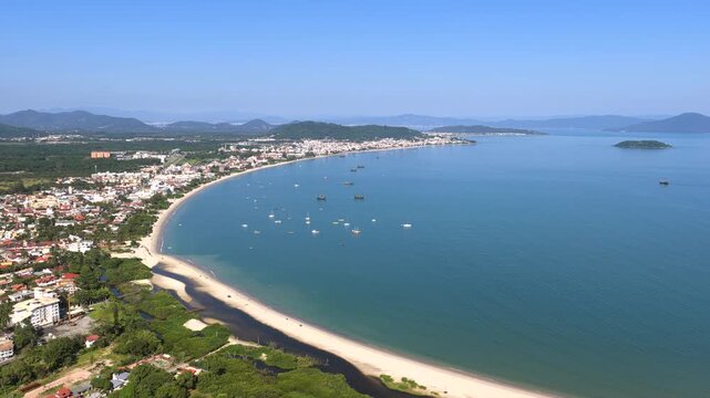 Coastal vegetation and houses at Cachoeira do Bom Jesus, looking at anchored yachts, sailboats and distant hills. Right tracking aerial.