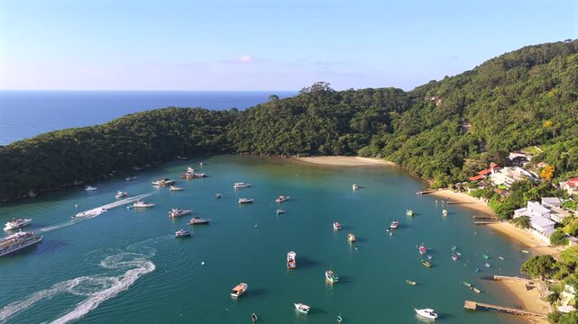 Anchored boats in Caixa D Aco beach Porto Belo Santa Catarina Brazil within sheltered bay bordered by Atlantic Forest vegetation and sandy cove under clear conditions, drone pullback reveal shot