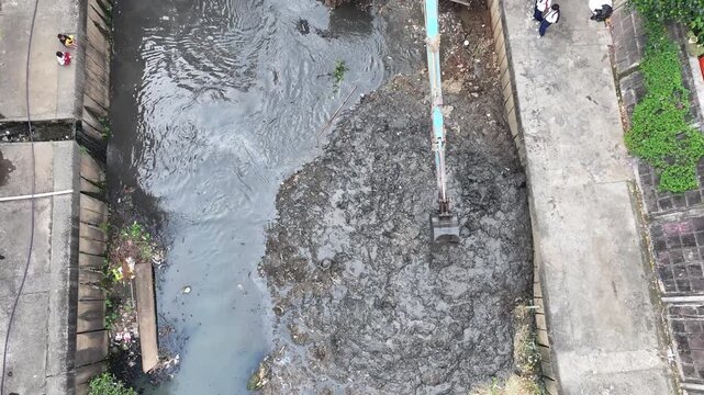 An blue excavator is working to digging the bottom of the jakarta river, Excavator with a long arm.  floating platform in a river digging cumulative dirt that shallowing the river