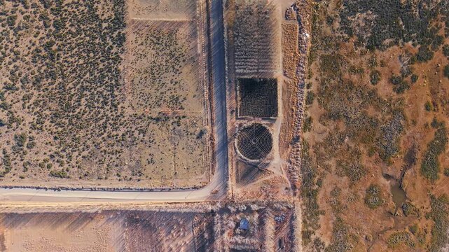 Top down drone view of a dirt road crossing dry countryside next to a circular hedge maze in Argentina.