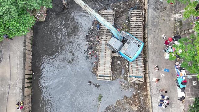 An blue excavator is working to digging the bottom of the jakarta river, Excavator with a long arm.  floating platform in a river digging cumulative dirt that shallowing the river