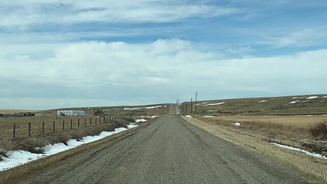 Wide angle POV driving across flat prairie terrain on unpaved road under expansive Alberta sky