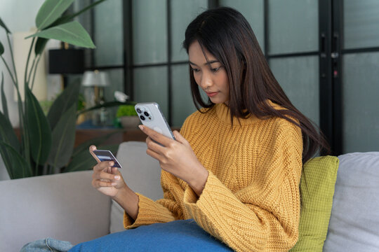 Asian woman sit on sofa using credit card online shoping on smartphone