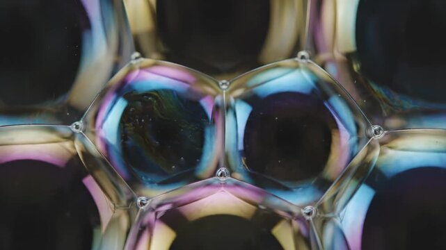 Dynamic macro shot of colorful soap bubbles creating intricate patterns and iridescent reflections on a dark background. Perfect for abstract and scientific themes.