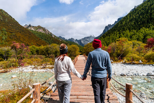 Rear view of a happy couple holding hands while walking across a wooden bridge in a mountain landscape and autumn forest
