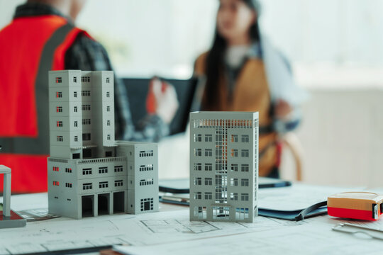 Architectural scale models on blueprint desk with blurred engineers meeting in background, concept of urban planning, construction project management and real estate development.