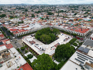 Obraz premium Aerial view of El Parian square, Tlaquepaque, Mexico. Colonial architecture, vibrant town life, and lush trees under an overcast sky.