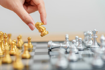 hand moving gold Chess knight figure and Checkmate opponent during chessboard competition. Strategy, Success, management, business planning, win, disruption, Trade war and leadership concept © Jo Panuwat D