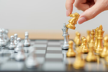 hand moving gold Chess knight figure and Checkmate opponent during chessboard competition. Strategy, Success, management, business planning, win, disruption, Trade war and leadership concept © Jo Panuwat D