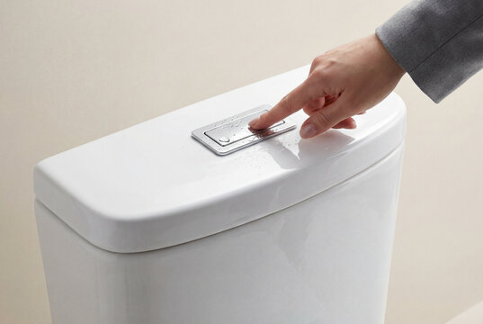 Hand pressing the silver flush button on the water tank of a clean modern white bathroom toilet