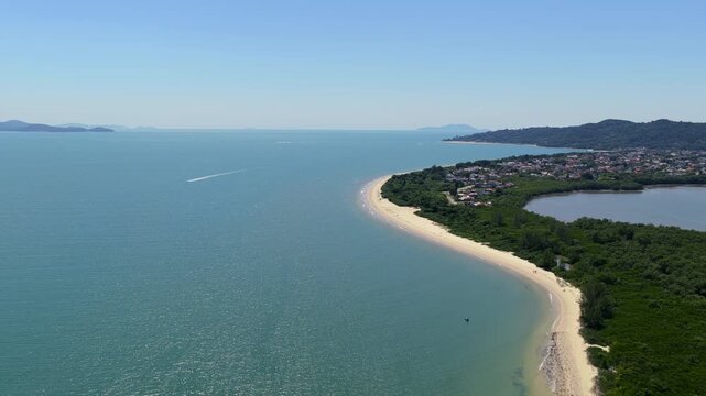 Praia da Daniela in Florian&oacute;polis Santa Catarina Brazil on Atlantic Ocean with curved sandbar separating Ba&iacute;a Norte from lagoon with vegetation and houses, drone lateral pan left