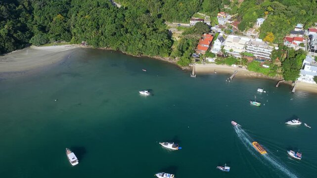 Aerial view of Caixa Daco beach in Porto Belo, Brazil, boats navigating turquoise bay with dynamic water trails.