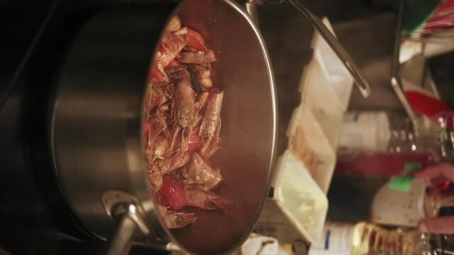Vertical video. Preparing meal. Culinary process. Chef hand adding soy sauce spicy powder to saucepan with vegetables seafood. Steaming stew asian prawn dish.