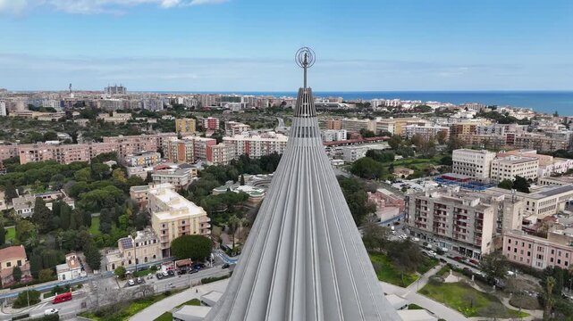 Drone orbit around Santuario della Madonna delle Lacrime in Syracuse, Sicily. Concrete brutalist architecture of the basilica with a panoramic view of the city and Ortigia in the distance.