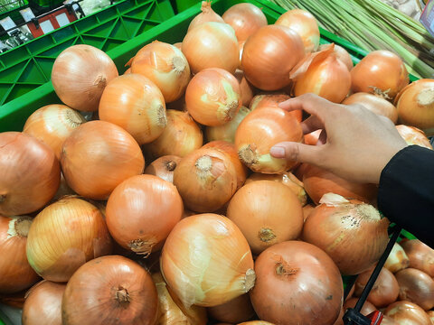 Women hand pick up onion in supermarket.