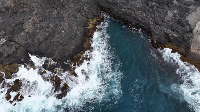 Birds-eye aerial view of powerful Atlantic waves crashing against the black volcanic rocks of Cruzinha, Santo Antao. Drone shot of white foam and deep blue sea in Cape Verde islands