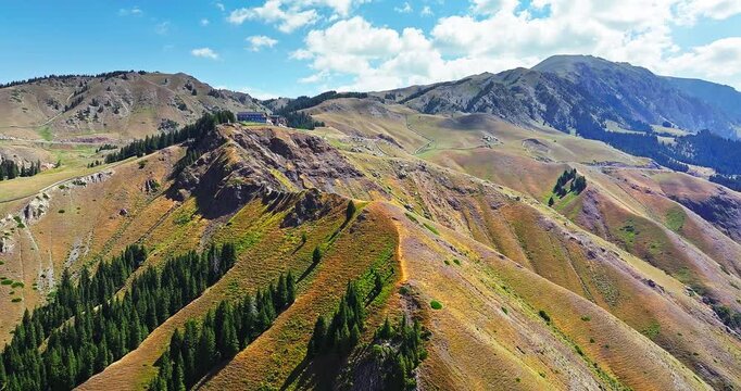 Aerial view of a mountain ridge with a building and evergreen trees under a cloudy sky in Xinjiang, China