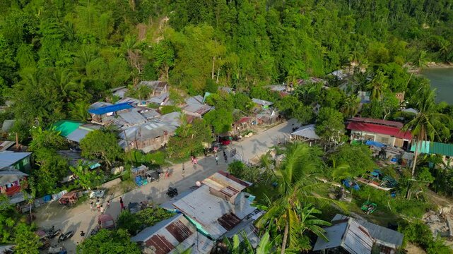 poor coastal village with children playing in the street, surrounded by simple homes and lush tropical vegetation. Great aerial view static panorama hovering drone