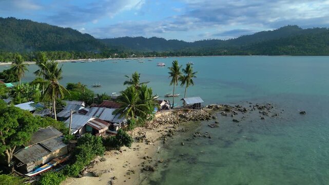 Fishing community living in simple housing along a sandy tropical beach, surrounded by lush vegetation and palm trees. speed ramp time lapse Magic aerial view fly reverse panorama drone