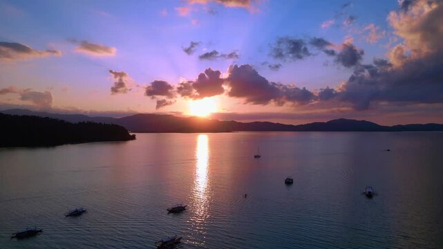 Traditional philipines outrigger bancas resting in a tranquil bay during an impressive colorful sunset, creating a peaceful tropical scene. Magic aerial view descending panorama drone