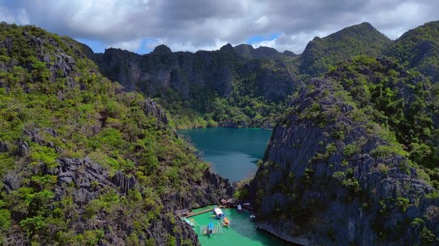 Barracuda Lake on Coron Island, Palawan, offering a unique dive spot. Lush green vegetation covers tall limestone cliffs surrounding the deep blue water. Fantastic aerial view ascending raise up pano