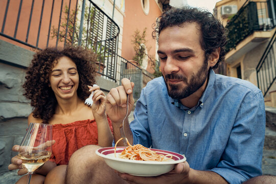 Young couple eating pasta and drinking wine outdoors in Italy