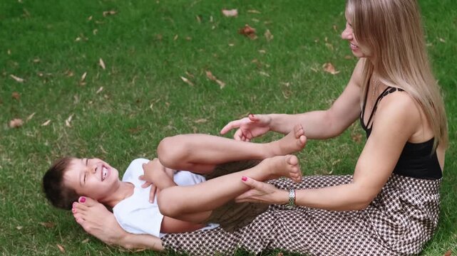 Summertime fun activity. Motherly affection. Happy positive woman laughing son together in green grass park engaging in playful tickling.