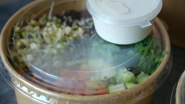 Healthy vegan salad packed in disposable craft paper bowl, fresh vegetables, mung bean sprouts, dressing, ready for takeout food delivery service, quick lunch. Healthy vegan salad bowl, takeaway lunch