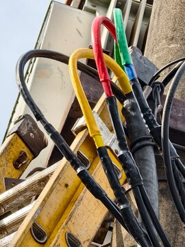 Electrical cable installation on a low to medium voltage distribution system with color-coded connections (red, yellow, green, black) indicating a three-phase power system. Visible insulated cable joi
