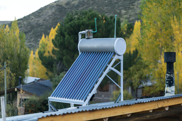 Solar water heater system installed on a rooftop with autumn trees in the background © Jezabel
