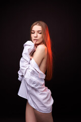 A young woman poses in a white off-the-shoulder shirt on a black background. The soft lighting highlights her relaxed and confident expression. She is wearing minimal underwear, which adds to her sens © SergeiPh