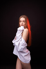 A young woman poses in a white off-the-shoulder shirt on a black background. The soft lighting highlights her relaxed and confident expression. She is wearing minimal underwear, which adds to her sens © SergeiPh