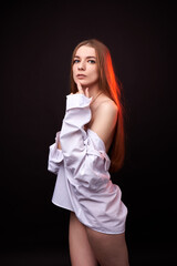 A young woman poses in a white off-the-shoulder shirt on a black background. The soft lighting highlights her relaxed and confident expression. She is wearing minimal underwear, which adds to her sens © SergeiPh