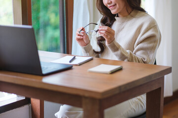 Closeup image of a woman holding glasses while working on laptop computer at home