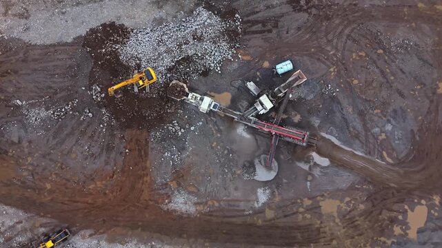 Top View aerial shot of a powerful stone crusher with vibrating screen working in a quarry in Nova Scotia, Canada. Mobile heavy equipment crushes stones for building industry near Halifax 4K.