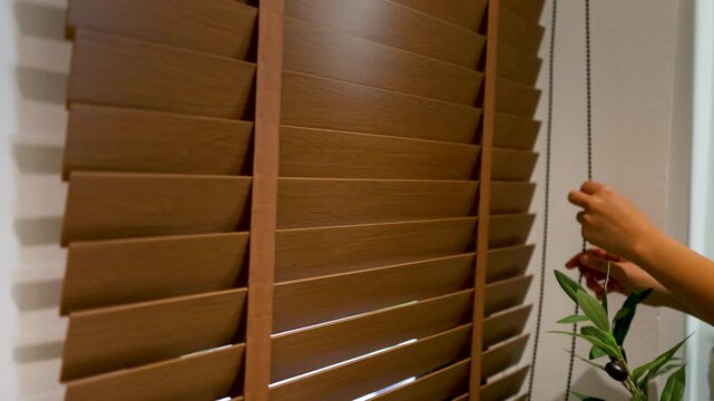 Hands Adjusting Wooden Venetian Blinds to Let Sunlight Into Room