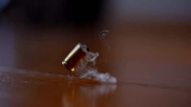 One bullet shell casing falling to the wooden surface in slow motion. Fired brass casing bouncing after shot, close up action detail.