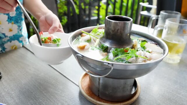 Serving Thai Seafood Tom Yum Soup from a Traditional Metal Hot Pot