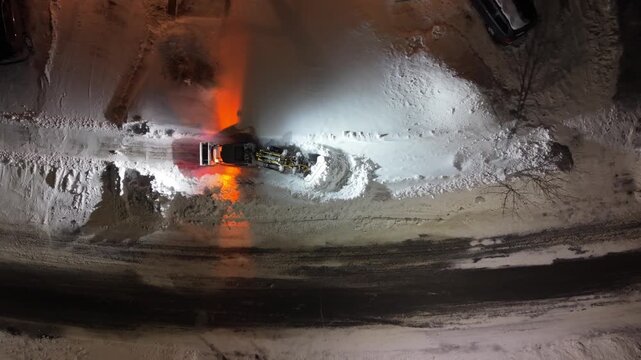 Top View aerial footage of a snowplow clearing accumulated snow from suburban streets in Beechville after heavy blizzard. Halifax area, Nova Scotia, Canada, winter maintenance at night 4K.