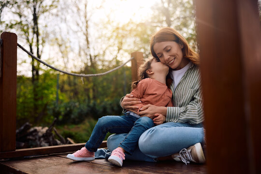 Loving little girl kissing her mother while enjoying in spring day in nature.