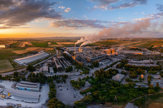 Industrial cement plant with smokestacks and agricultural fields at sunset, wide angle view from above