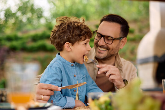 Little boy being feed by his father while having lunch on patio.