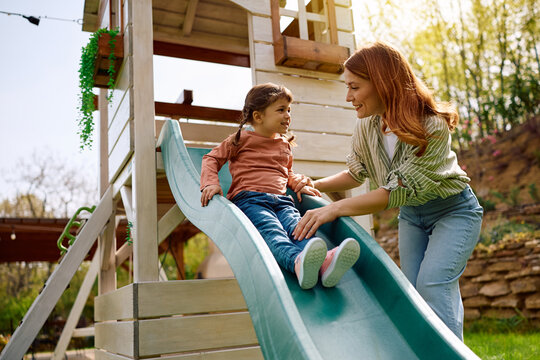 Happy little girl sliding while spending spring day at playground with her mother.