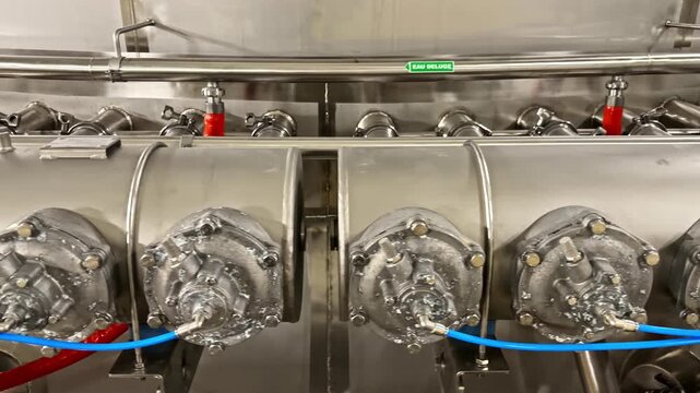 Panning shot of automated industrial equipment in dairy factory featuring stainless steel valves and pneumatic tubes for food processing