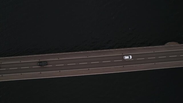 Dramatic top down aerial shot following cars driving on the Skye Bridge, a vital concrete connection over the dark waters of Loch Alsh