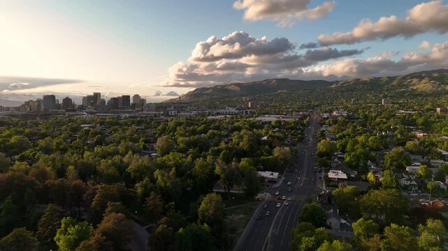 Aerial drone view of Morgantown showing city skyline, long road with traffic, dense green trees, and distant hills under warm evening light and scattered clouds