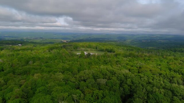 Aerial drone view of dense forest and rolling hills near Rock of Cashel in Tipperary, showing wide green landscape, distant fields, and dramatic cloudy sky