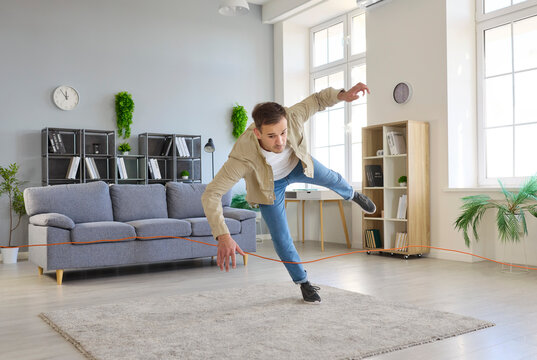 Accident of tripping over cord at home, home hazard for man walking to trip and fall on living room floor. Young clumsy person falling on carpet by sofa with unsafe risk of injury, stumble over wire