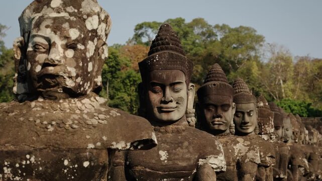 Row of ancient stone figures aligned along temple bridge pathway in Cambodia